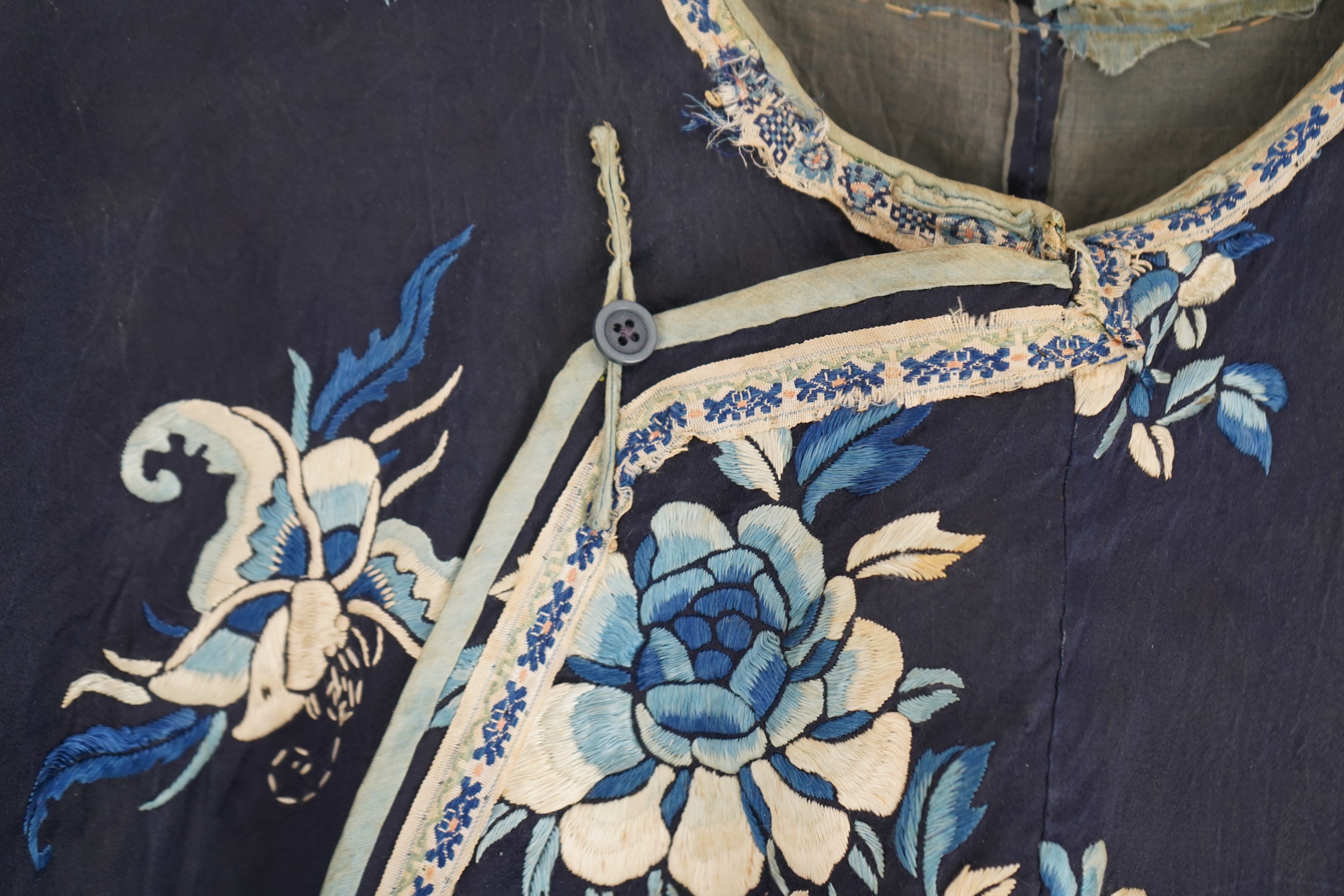 An early 20th century blue silk embroidered Chinese child’s robe, embroidered with bats and flower motifs, bordered with rows of silk braid. Condition - the original silk lining has been removed, it may benefit from bein